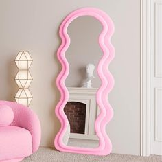 a pink mirror sitting on top of a floor next to a chair and fire place