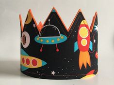 a black crown with colorful rockets and stars on the front, sitting on a white surface