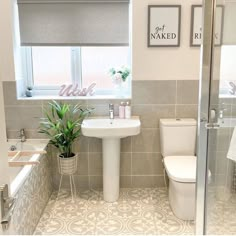 a white toilet sitting next to a bath tub under a bathroom window near a sink