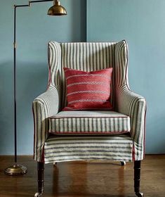 a striped chair with a red pillow in front of a blue wall and floor lamp