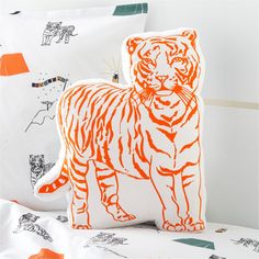 an orange and white tiger pillow sitting on top of a bed next to two pillows