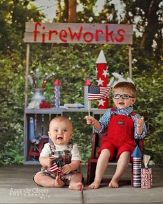 two young boys sitting on the ground with fireworks in front of them and a fire works sign behind them