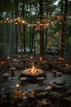 a fire pit in the middle of a forest with lights strung from it's sides