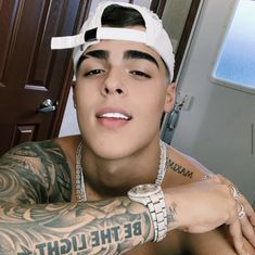 a young man with tattoos on his arm and chest wearing a white hat, sunglasses and bracelet