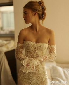 a woman in a wedding dress is standing near a bed and looking off to the side