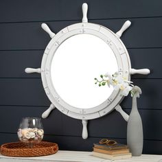 a white ship wheel mirror sitting on top of a table next to a vase with flowers