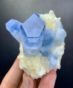 a hand holding some kind of rock with blue and yellow crystals on it's surface