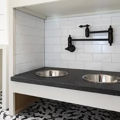 two stainless steel sinks in a black and white tiled kitchen with an overhead faucet