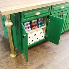 a green kitchen island with two rolls of toilet paper in the bottom drawer and gold handles