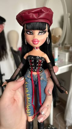 a hand holding a doll with black hair and red lipstick on it's face