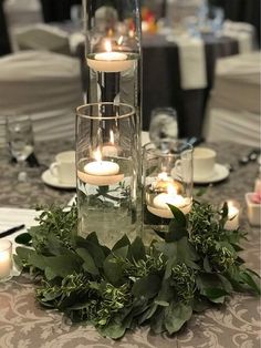 candles are lit in glass vases with greenery