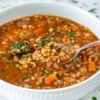 a white bowl filled with lentula soup and topped with parsley on the side