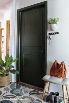 a black door in a white room next to a chair and potted plant on the floor