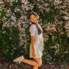 a young woman is posing in front of some bushes and flowers with her legs spread out