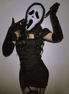 a woman in a black dress with a mask on her face and holding a knife