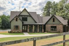 a large house sitting on top of a lush green field next to a lake in front of a wooden fence