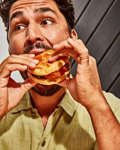 a man eating a large sandwich in front of his face and looking up at the camera