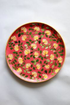 a red plate with yellow and green flowers painted on the side, sitting on a white surface