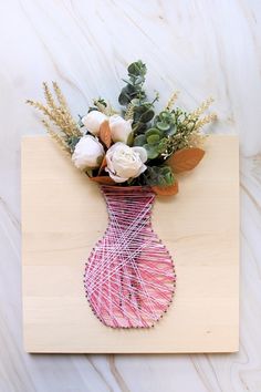 a pink vase with white flowers and greenery on a wooden board that has string wrapped around it