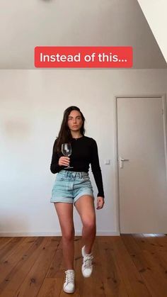 a woman standing in an empty room holding a wine glass and looking at the camera