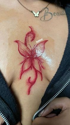 a woman with tattoos on her chest has a red flower painted on her chest piece