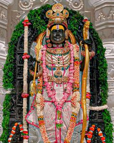 the statue is decorated with flowers and garlands on it's head, surrounded by greenery