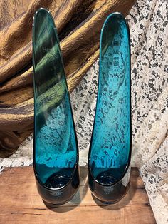 two blue glass vases sitting on top of a wooden table next to a curtain