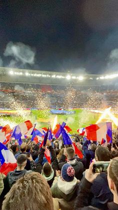 a crowd of people at a soccer game holding flags and confetti in the air