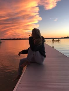 a woman sitting on the end of a pier at sunset