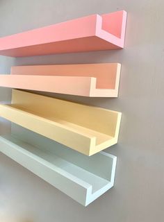 three shelves on the wall are painted different shades of pink, yellow and white with one shelf below them