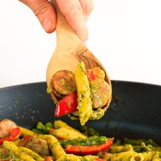 a wooden spoon scooping some food out of a skillet filled with pesto pasta