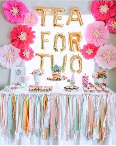 a table topped with lots of paper flowers and balloons in the shape of letters that spell out tea for two