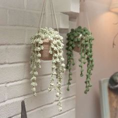 three hanging baskets with plants in them on a brick wall next to a mirror and lamp