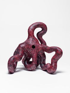 a red sculpture sitting on top of a white table next to a black object in the shape of an octopus