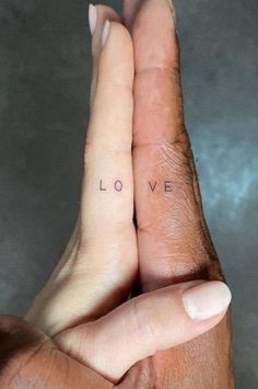 two hands holding each other with the word love tattooed on their thumbnails in front of them