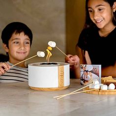 two young children sitting at a table with marshmallows in front of them