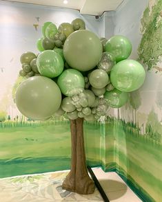 a tree made out of balloons sitting in front of a wall with a painting on it