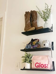 two black shelves with shoes, plants and other items on them in the corner of a room