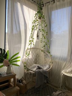 a hanging chair in front of a window with curtains and plants on the windowsill