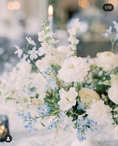 a vase filled with white and blue flowers on top of a table next to candles