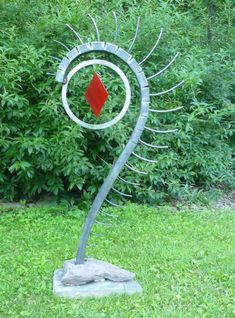 a metal sculpture in the grass with a red diamond on it's back end