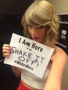 a woman holding up a sign that says i am here to shake it off