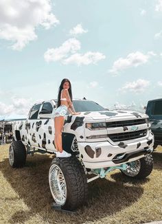 a woman is sitting on the hood of a white truck with cow print paint job