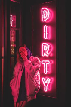 a woman standing in front of a neon sign with the word dirty written on it