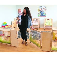 a woman holding a baby in her arms while standing next to wooden playpens