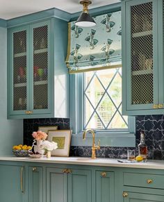 a kitchen with blue cabinets and marble counter tops in front of a window that has gold trim