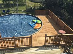 an above ground pool surrounded by wooden decking and fenced in area with water toys