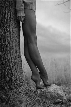 a person standing next to a tree with their bare legs on top of a rock