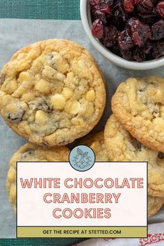 three white chocolate cranberry cookies next to a bowl of cherries