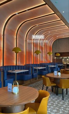 the interior of a restaurant with blue and yellow chairs, wooden tables and gold lamps